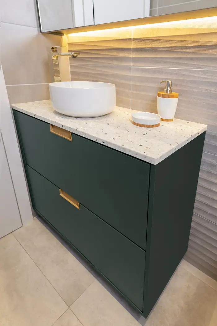Gabinete verde com puxador dourado e bancada de granilite