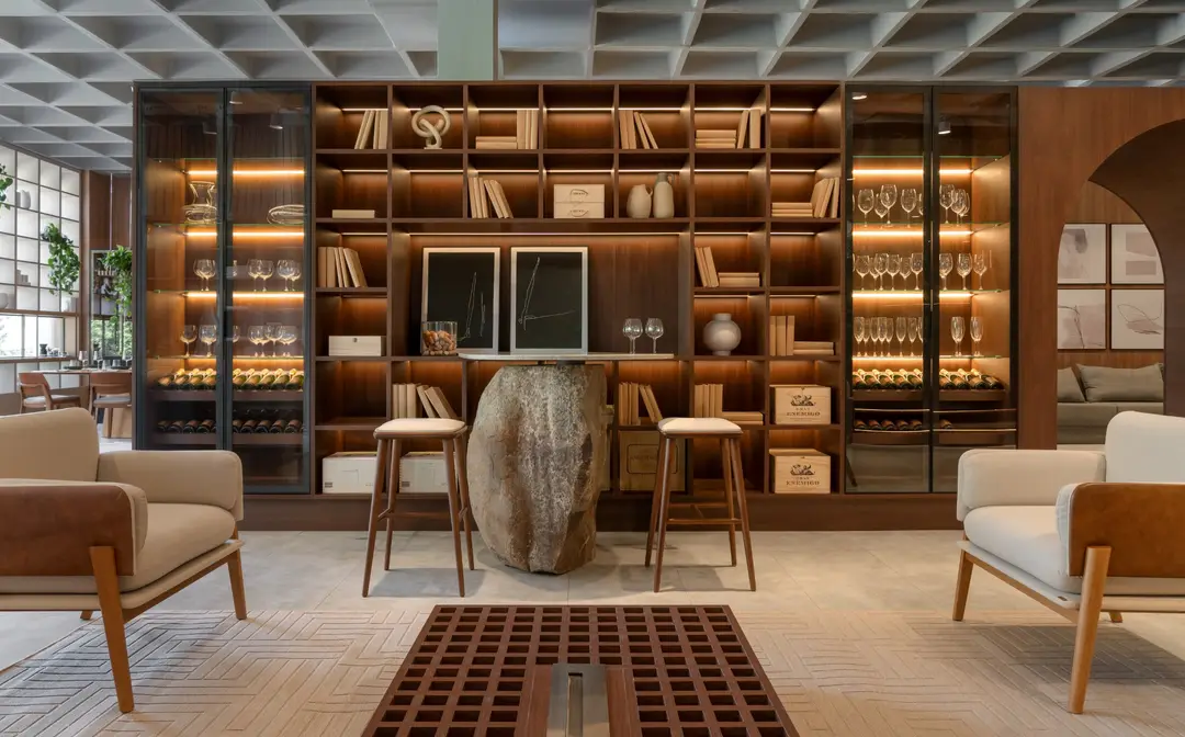 Ambiente de estar com adega, biblioteca iluminada e poltronas em madeira